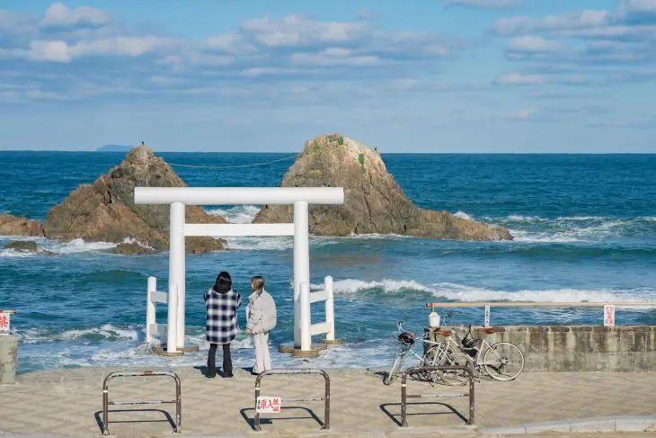 福岡県糸島市の景勝地「桜井二夫婦岩」と海に立つ白い鳥居を眺める観光客