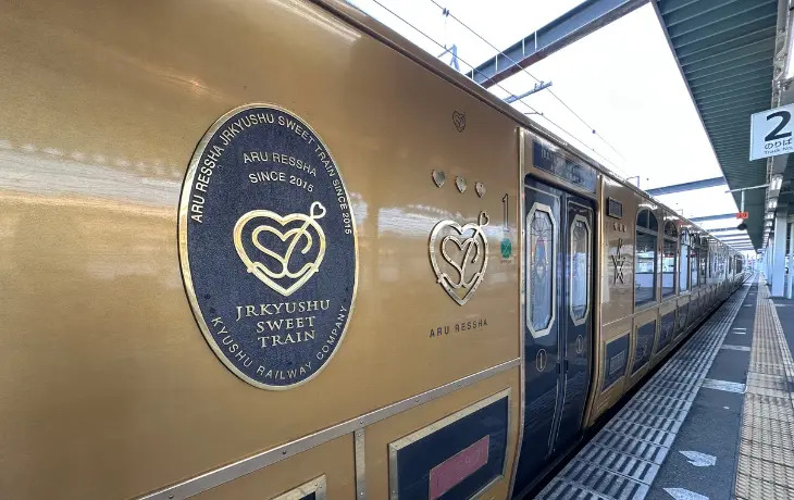駅ホームに停車するJR九州の観光列車「或る列車」の金色の車体とロゴエンブレム