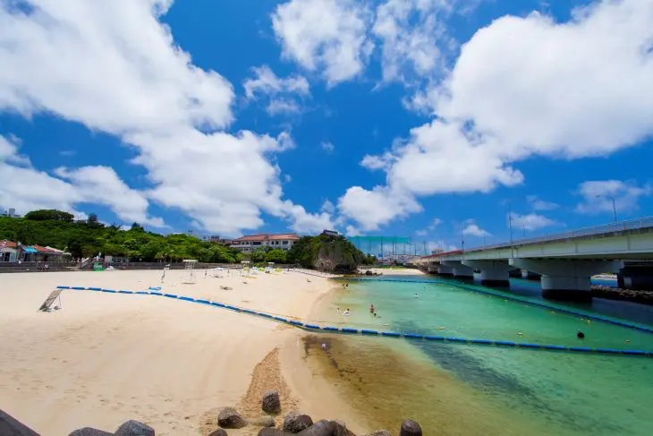 快晴の空のもと、美しいエメラルドグリーンの海と白い砂浜が広がる沖縄のビーチ。