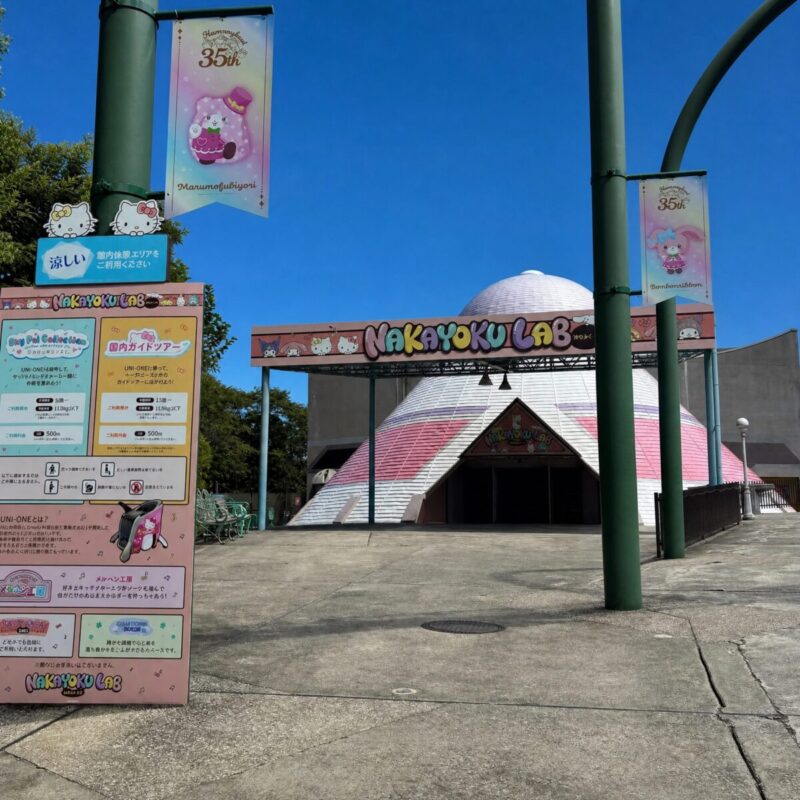 快晴の青空とドーム型の「NAKAYOKU LAB」外観。手前に35周年フラッグの柱と案内看板が立っています。